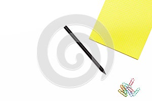 Yellow Notepad and a black pencil with paper clips on a white background. Minimal working concept for office Desk