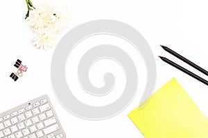 Yellow Notepad, computer keyboard, paper clips, two black pencil and a chrysanthemum flower on a white background. Minimal busines