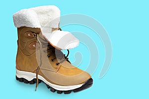 Yellow nubuck boot, with white fur, on a turquoise background, shoes unlaced, concept, isolate