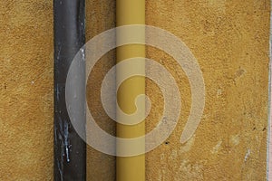 Yellow ochre plastered wall with drainpipes, brown and yellow