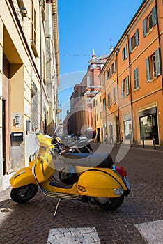 Yellow old fashioned scooter on street in Rimini with many-coloured houses, ancient city center. Vacation in beautiful Italy,