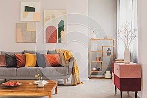 Yellow, orange, black and brown pillows on comfortable grey scandinavian sofa in bright living room interior with abstract