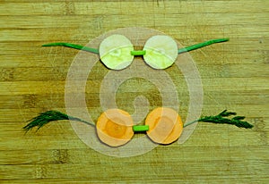 Yellow and orange carrots cut into circles in the form of eye glasses and green arcs on a wooden cutting board