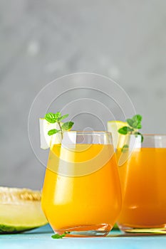 Yellow orange cocktail with melon and mint in glass on blue concrete background, close up