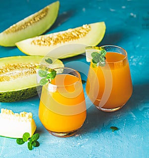 Yellow orange cocktail with melon and mint in glass on blue concrete background, close up. Summer drinks and alcoholic cocktails.