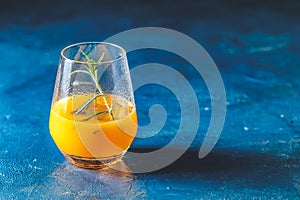 Yellow orange cocktail with tangerine and rosemary in glass on dark blue concrete background, close up. Christmas and New Year