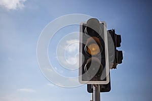 Yellow, orange color traffic light. Blue sky with few clouds background. Close up under view, copyspace.
