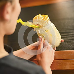Yellow orange and lemon freakshake with sweets. Eating out concept. Young attractive woman drinking freak shake