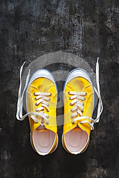 yellow-orange sneakers with untied laces on a dark concrete background. Copy space. View from above