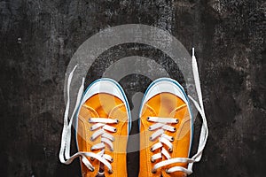 yellow-orange sneakers with untied laces on a dark concrete background. Copy space. View from above