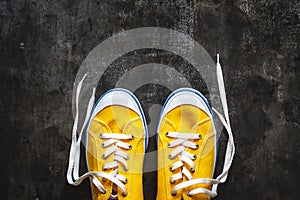 yellow-orange sneakers with untied laces on a dark concrete background. Copy space. View from above