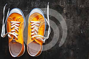 yellow-orange sneakers with untied laces on a dark concrete background. Copy space. View from above