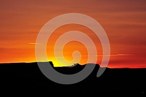 Yellow-orange sunset above black silhouette of mesas in Utah