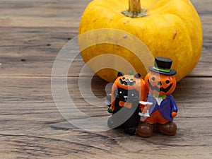 Yellow organic pumpkin and orange miniature ceramic pumpkin guy with black cat on dark wooden background