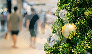 Yellow ornament on pine tree at department store with copyspace of people walking and shopping in background, Christmas and New