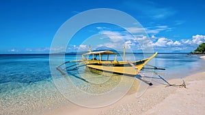 A yellow outrigger boat anchored in crystal clear water off a white sand beach in the Philippines.