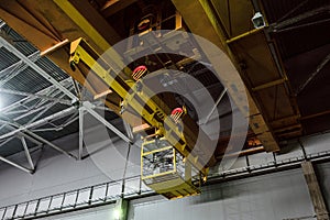 Yellow overhead crane with linear traverse and hooks in engineering plant shop