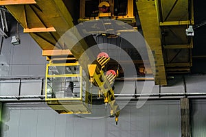 Yellow overhead crane with linear traverse and hooks in engineering plant shop