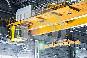 Yellow overhead crane with linear traverse and hooks in engineering plant shop