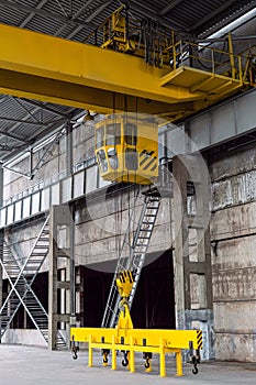 Yellow overhead crane with linear traverse and hooks in engineering plant workshop