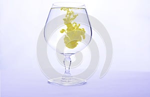 Yellow paint in water in a crystal glass on a white background