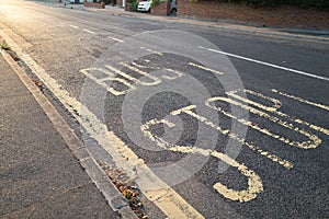 Yellow painted bus stop sign on a residential road on a summer evening as the sunlight illuminates the tarmac. The focus is