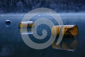 yellow painted old rusty oil barrels float on a lake in winter