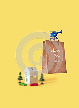 Yellow paper bag gift toy house tree delivery helicopter fly copy space background I love you mom