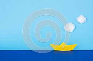Yellow paper boat moving on blue sea with sky and clouds