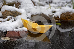 Yellow paper boat stuck in the ice, on a frozen puddle