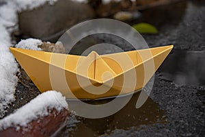 Yellow paper boat stuck in the ice, on a frozen puddle