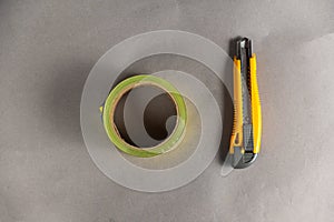 Yellow paper cutter and adhesive tape. The hand tool lies on a gray uneven surface. Blue and yellow duct tape. Top view. Copy