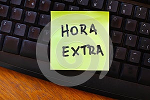 A yellow paper note with hora extra phrase on a black computer keyboard