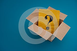 Yellow paper note with question mark inside an open cardboard box