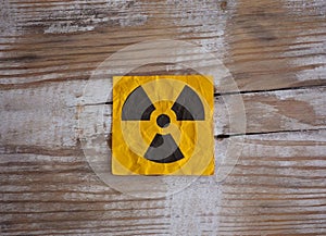 A yellow paper note with Radiation warning sign on it on a wooden surface.