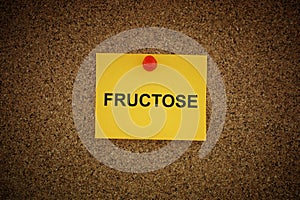 A yellow paper note with the word Fructose on it pinned to a cork board