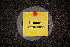 A yellow paper note with the words Human Trafficking on it pinned to a cork board