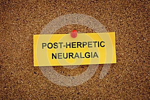 A yellow paper note with the words Post-Herpetic Neuralgia on it pinned to a cork board