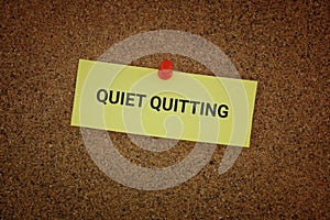 A yellow paper note with the words Quiet Quitting on it pinned to a cork board