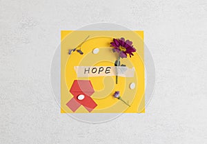 Yellow paper with red ribbon, gerberas, the word hope and pills on stone.