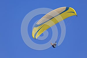 A yellow paraglider gliding across a clear blue sky