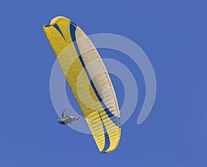 A yellow paraglider gliding across a clear blue sky