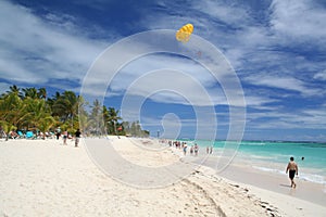 Yellow Paraglider hangs over sunbathers on white Caribbean beach