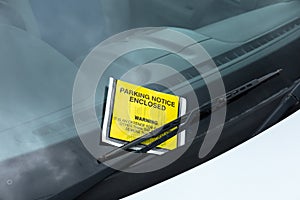 Yellow parking enforcement ticket stuck to car windscreen