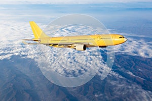 Yellow passenger plane is flying over the clouds. Side view of aircraft