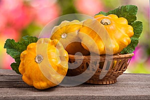 Yellow pattypan squash with leaf in a wicker basket on wooden table blurred background