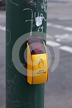 yellow pedestrian crossing button on green pole with icon of hand and red text above: Signal kommt, which means Signal
