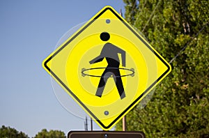 A yellow pedestrian crosswalk sign with a hula hoop drawn onto it.