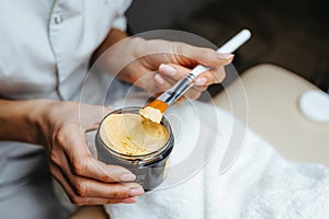 Yellow peeling cream with a brush and a cosmetologist`s hands