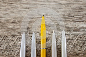 Yellow pen in the middle of white on a wooden background. Stand out, think differently. individuality and leadership